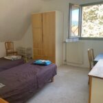 This spacious bedroom features two comfortable single beds, a large wardrobe, a desk and plenty of natural light. It provides a peaceful and practical living space for students sharing their homestay experience.