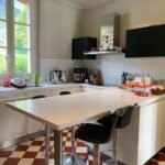 Modern white family kitchen with central island, breakfast stools, and large window overlooking the garden.