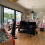 Bright family living room with piano, foosball table, wooden floors, and access to the terrace.