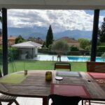 Covered outdoor dining area overlooking a swimming pool and mountains near Grenoble.